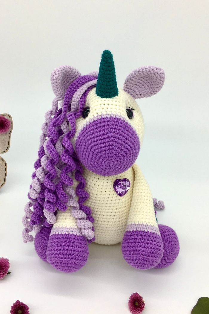 A Crocheted Stuffed Unicorn Sitting Next To Flowers